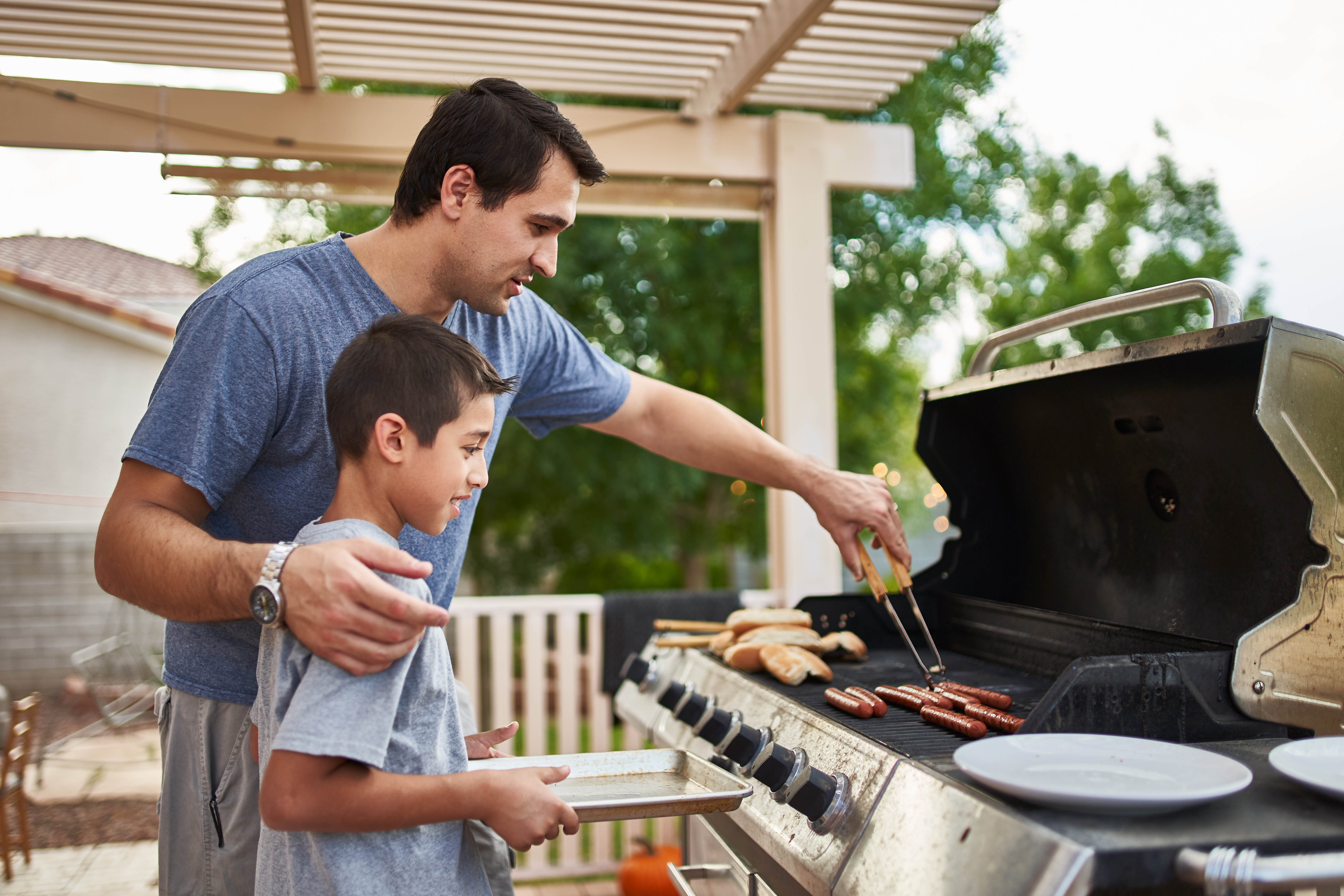 Dad getting food off the barbecue for his young son